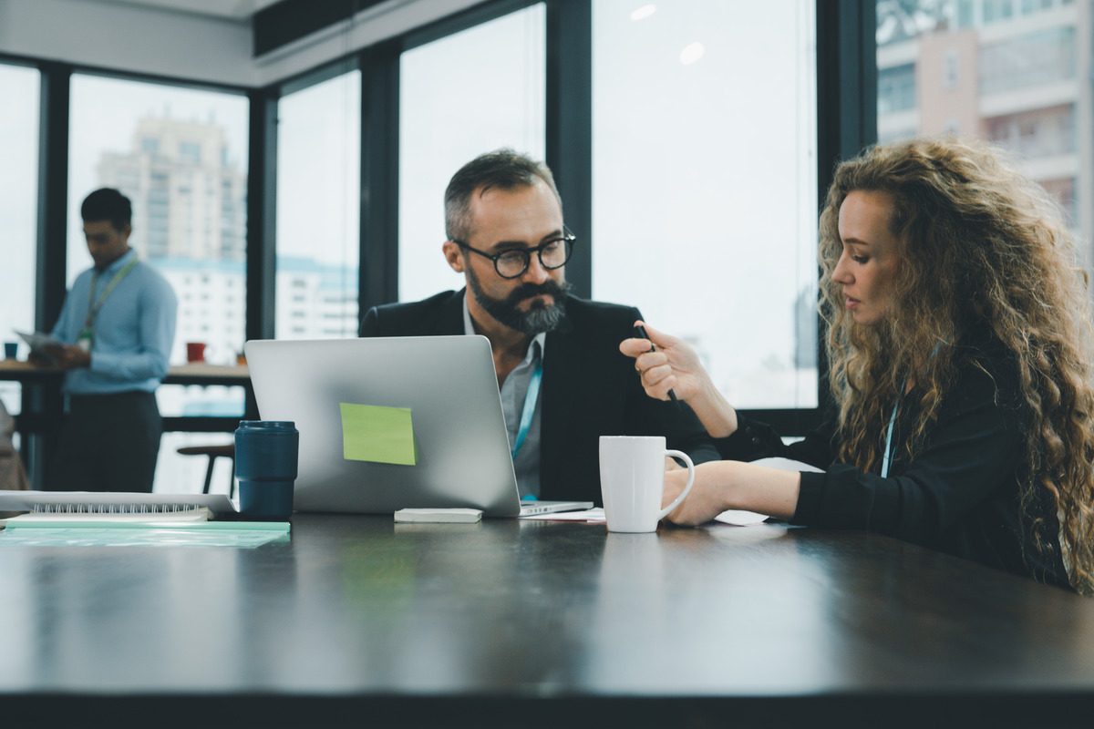 Two people sitting at a table in an office setting looking at a laptop screen