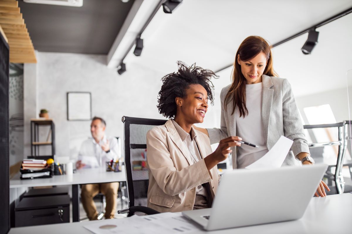 two women working at a desk over a laptop